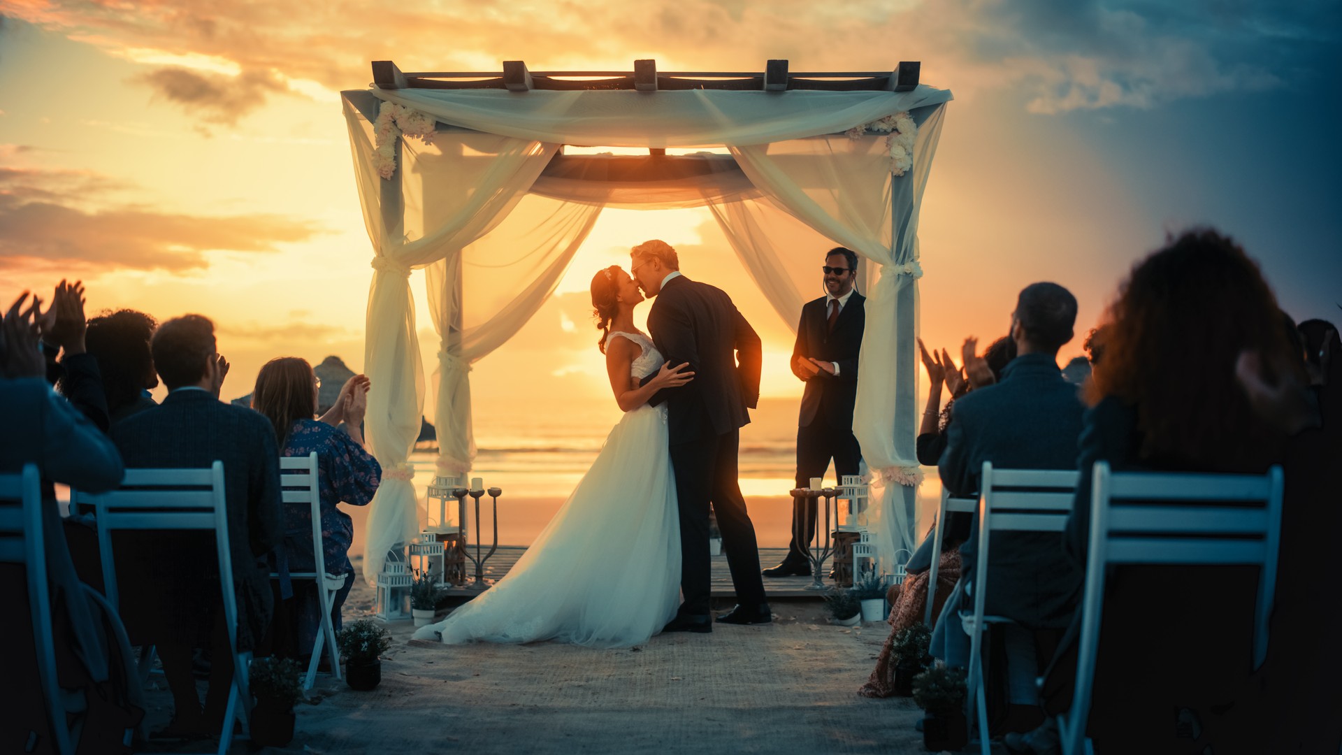 Schöne Braut und Bräutigam während einer Hochzeitszeremonie im Freien an einem Meeresstrand bei Sonnenuntergang. Perfekter Ort für romantische Paare, um zu heiraten, Ringe auszutauschen, zu küssen und Feiern mit Freunden zu teilen.