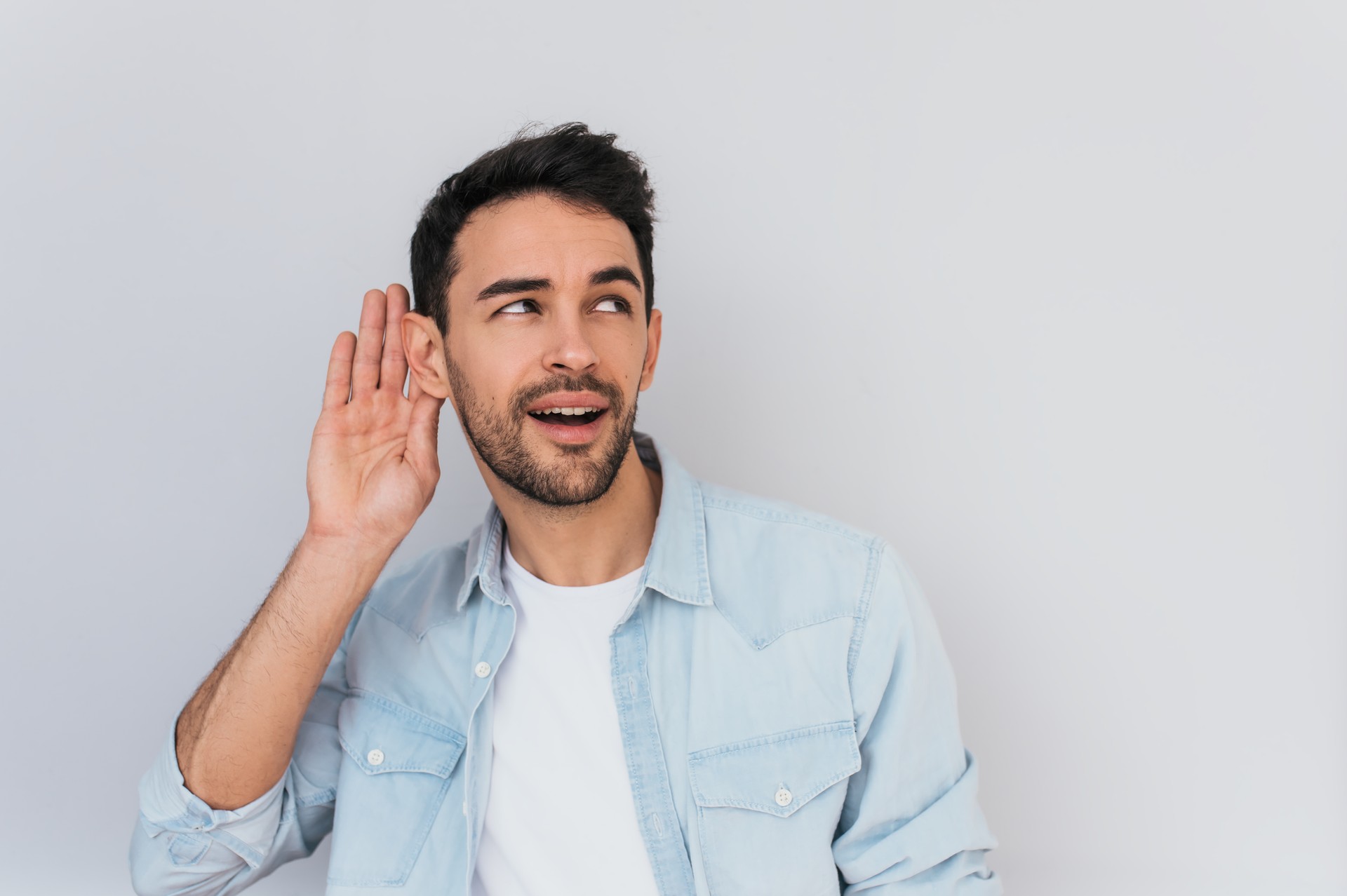 Porträt der schönen interessiert männlich er Hand am Ohr, jemanden zu sprechen, isoliert auf weißem Hintergrund. Stilvolle Jüngling das Gespräch im Studio belauscht. Platz für Text zu kopieren.